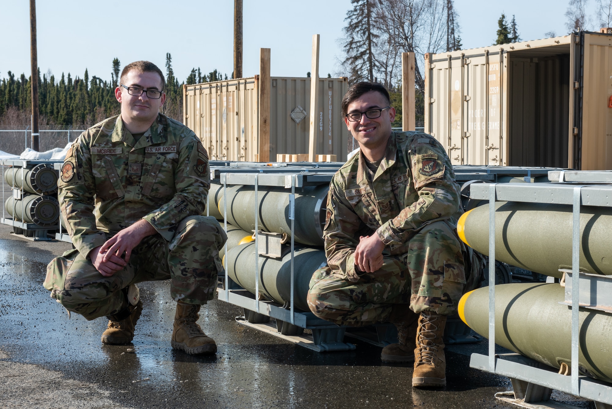 A photo of two Airmen pausing for a photo next to munitions.