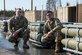 A photo of two Airmen pausing for a photo next to munitions.