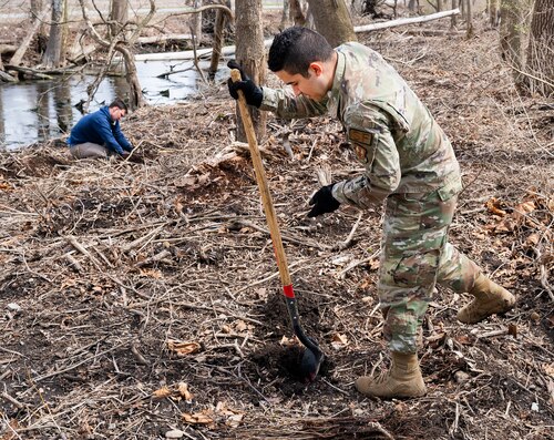 Staff Sgt. Miguel Ramos (foreground) and Staff Sgt. Paul Jazowski, both with the 88th Security Forces Squadron, plant seedlings April 7, 2022, along Trout Creek on Wright-Patterson Air Force Base, Ohio. The two were part of a group that planted 180 seedlings of native trees along the creek near Huffman Prairie as part of the base’s observance of Earth Day. (U.S. Air Force photo by R.J. Oriez)