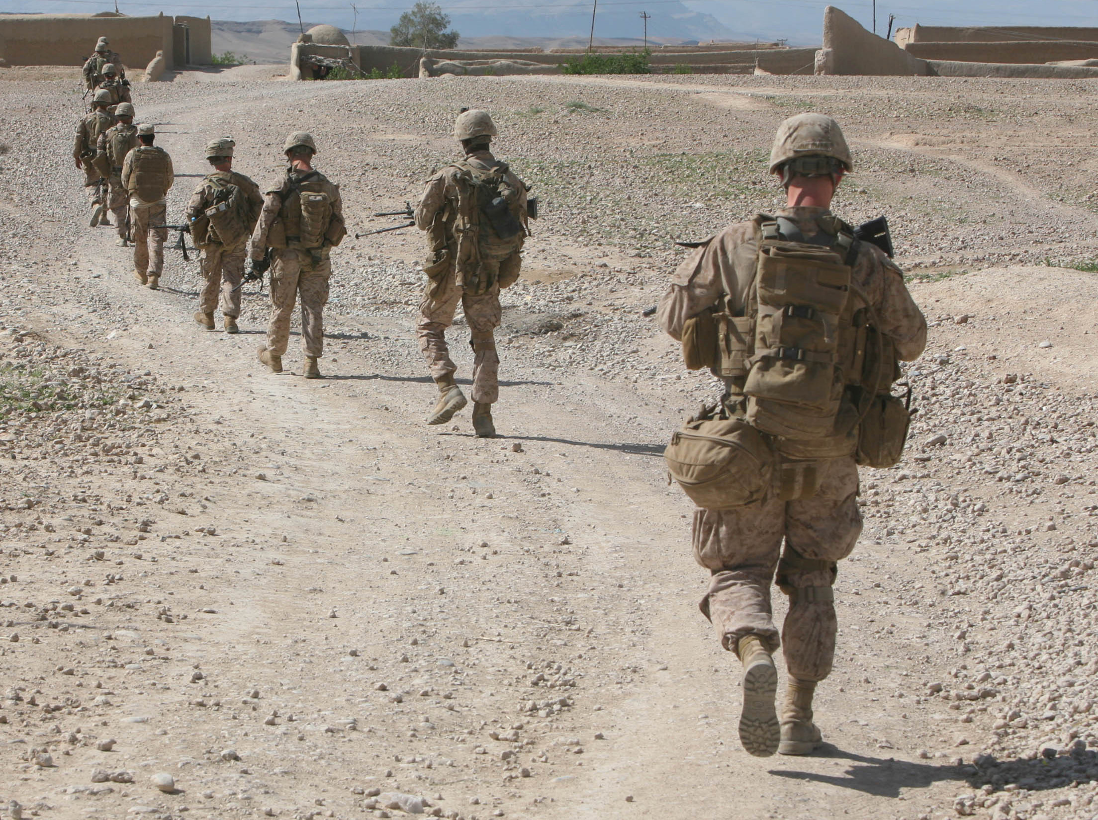 Marines in combat uniform walking in a line in the desert.