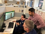 Three Coast Guard employees working in cubicle space