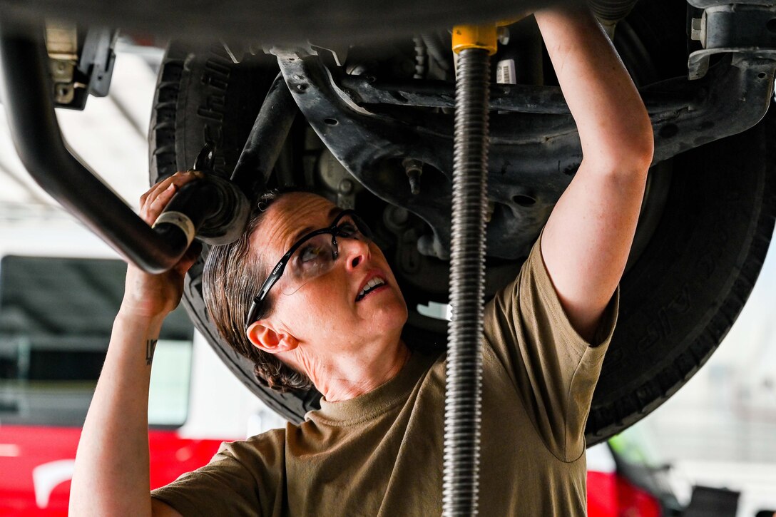An airman works on the undercarriage of a truck.