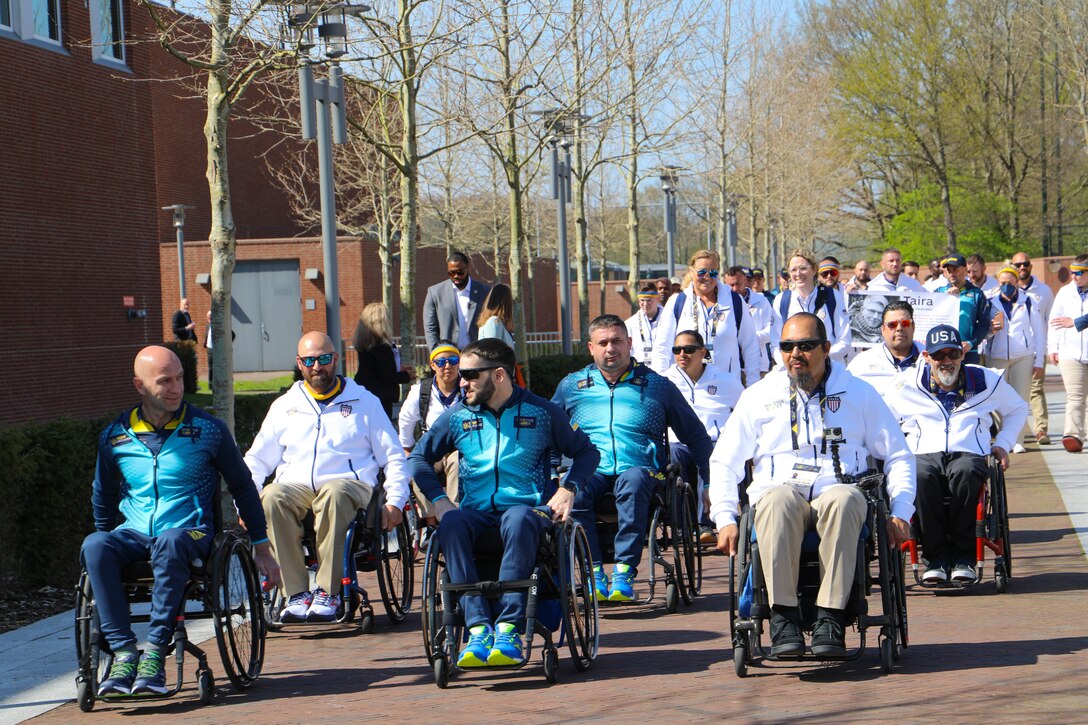 A group of athletes, some in wheelchairs, travel along a paved walk.