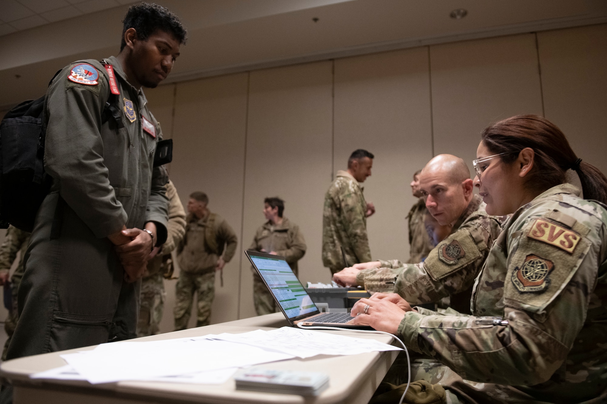 U.S. Air Force Airman 1st Class Neysha Quinones Serrano, right, 60th Force Support Squadron services specialist, checks in Senior Airman Ezekiel Smith, 22nd Airlift Squadron loadmaster, into lodging at the Alpena Combat Readiness Training Center, Alpena, Michigan, April 10, 2022. Serrano is sitting at a table as Smith stands.