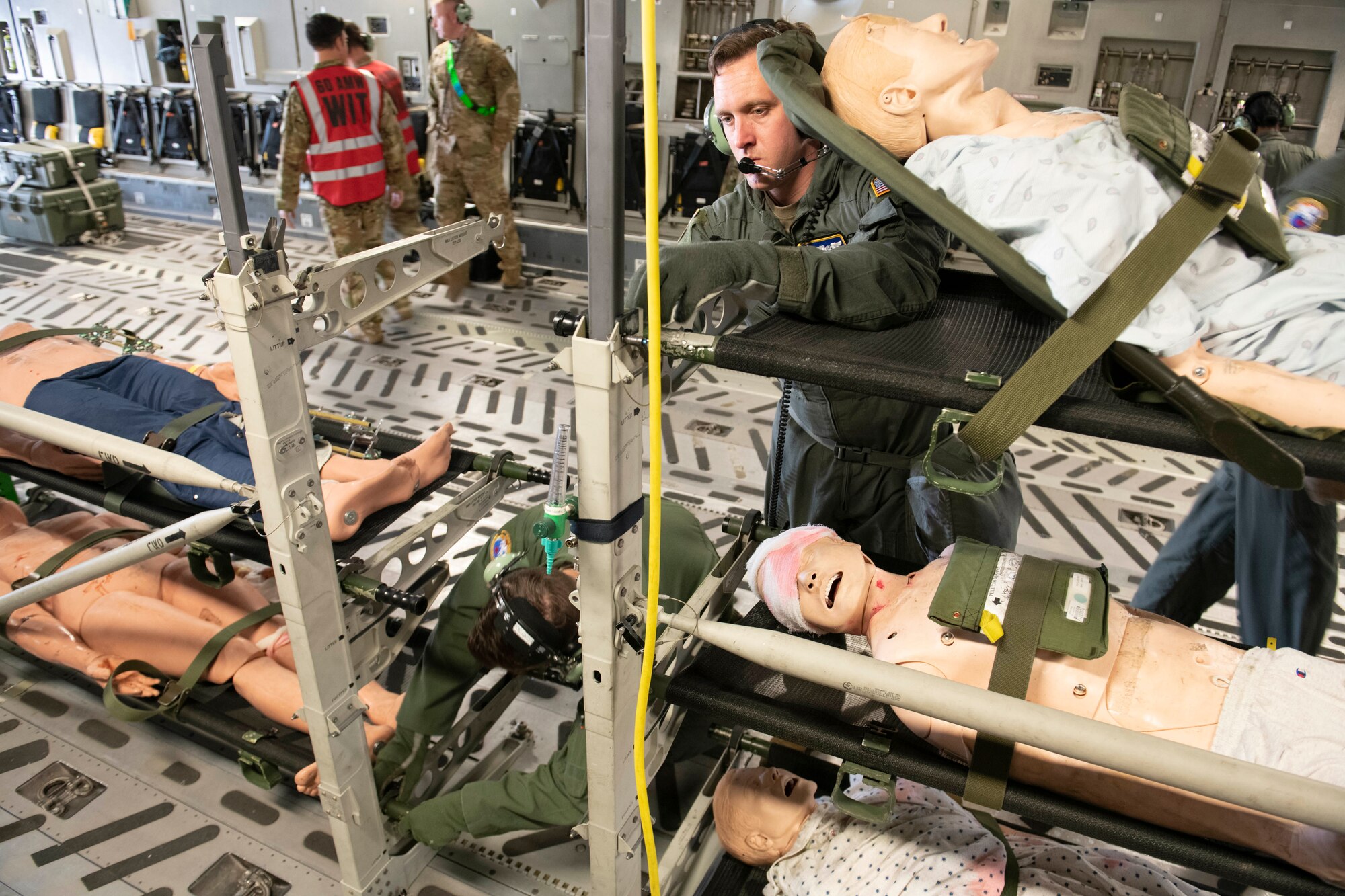 U.S. Air Force Staff Sgt. Michael Hauptman, right, 60th Aeromedical Evacuation Squadron AE technician, finishes setting up a stanchion litter system inside a C-17 Globemaster III from Travis Air Force Base, California, at the Alpena Combat Readiness Training Center, Alpena, Michigan, April 11, 2022. There are five simulated patients in stanchions.