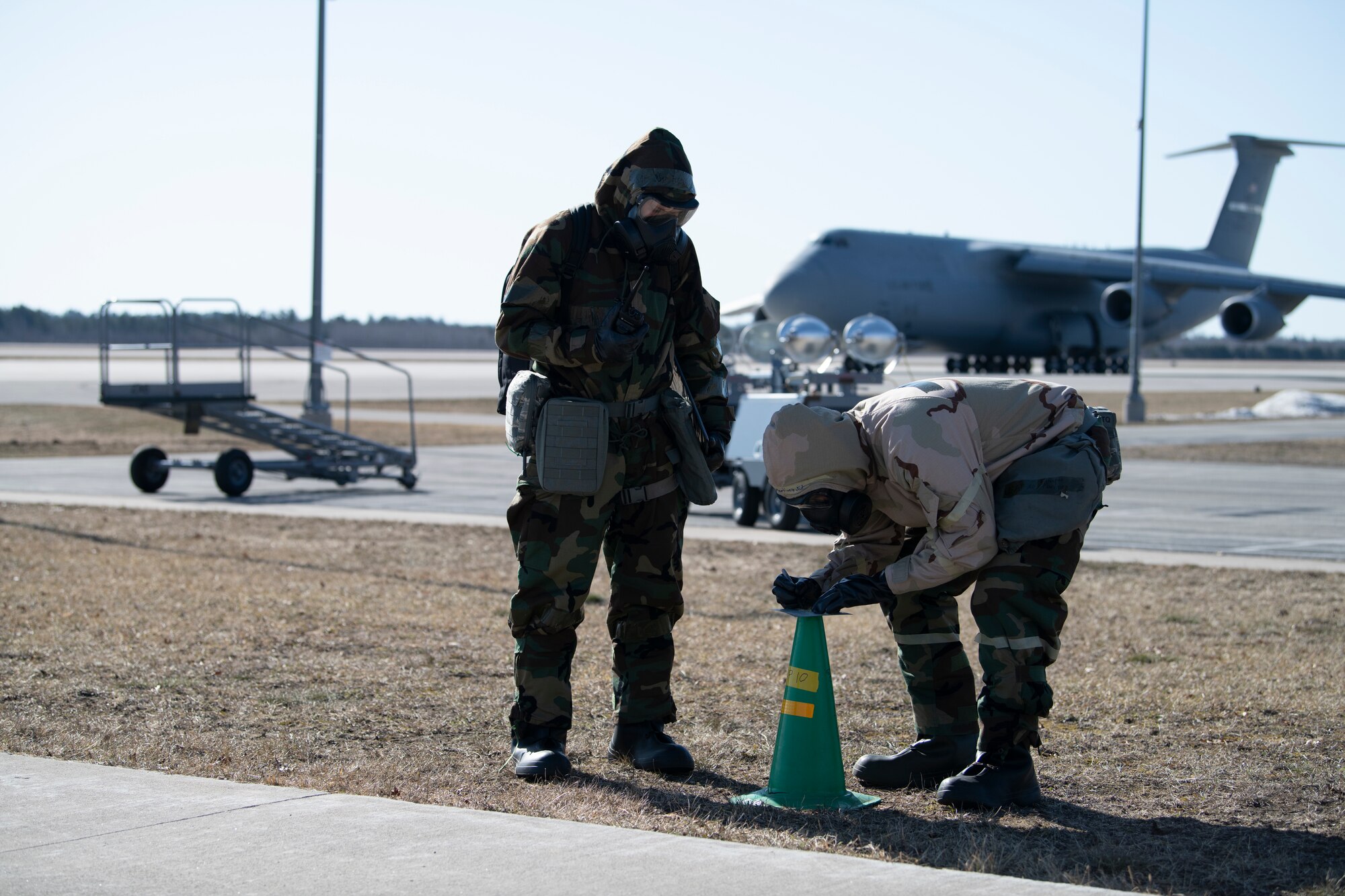 U.S. Air Force Staff Sgt. Jordan Harris, left, 60th Maintenance Squadron aero repair team leader, and Airman 1st Class Eduardo Martinez, 60th MXS aero repair team member, conduct a post-attack reconnaissance after a simulated chemical attack at the Alpena Combat Readiness Training Center, Alpena, Michigan, April 12, 2022. The Airmen are wearing MOPP gear while checking M8 paper on a cone.