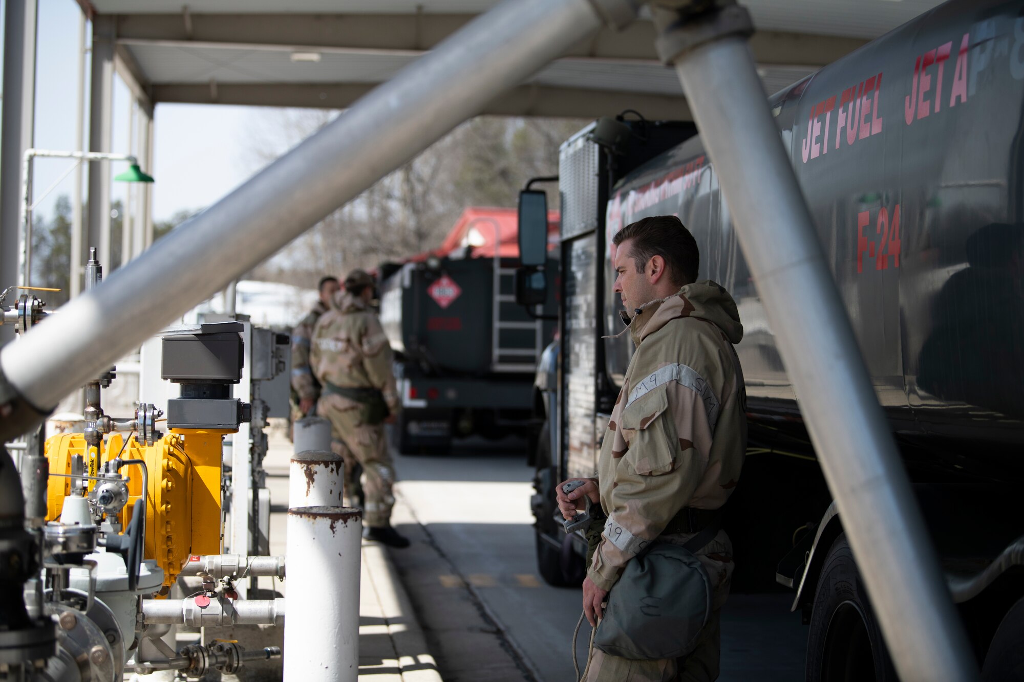 U.S. Air Force Staff Sgt. Casey Bonillas, 60th Logistics Readiness Squadron ground transportation specialist and non-commissioned officer in charge of equipment support, refuels an R-11 fuel truck while donned with mission-oriented protective postures (MOPP) gear at the Alpena Combat Readiness Training Center, Alpena, Michigan, April 12, 2022. Bonilas is standing next to the back end of the truck and watching a gauge as he refuels the truck.