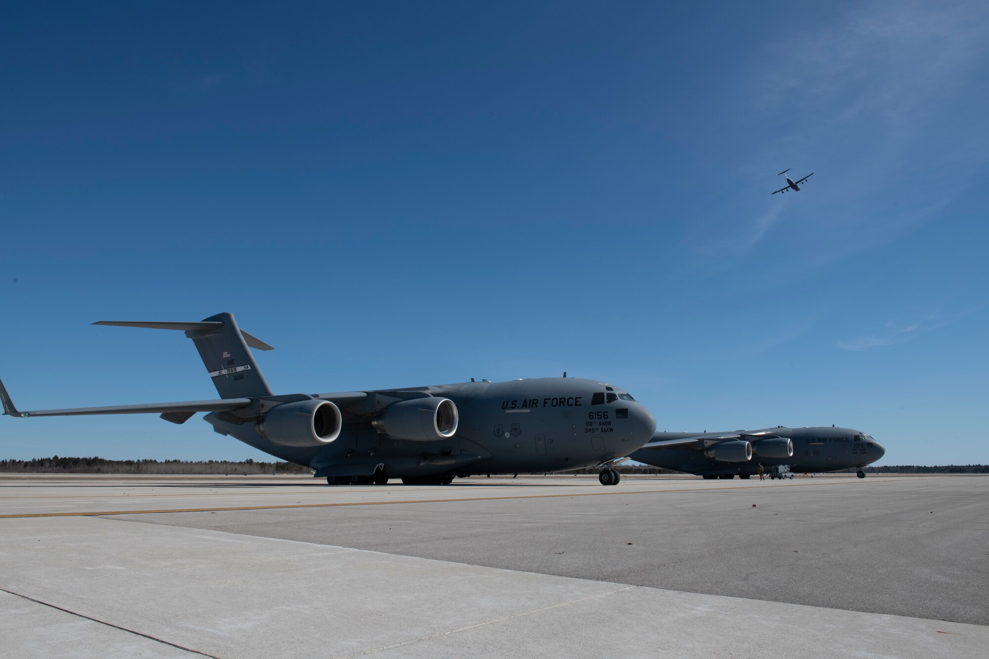 U.S. Air Force C-17 Globemaster III aircraft from Travis Air Force Base, California, are parked on the flight line at the Alpena Combat Readiness Training Center, Alpena, Michigan, April 10, 2022, while a Travis C-5M Super Galaxy flies above.