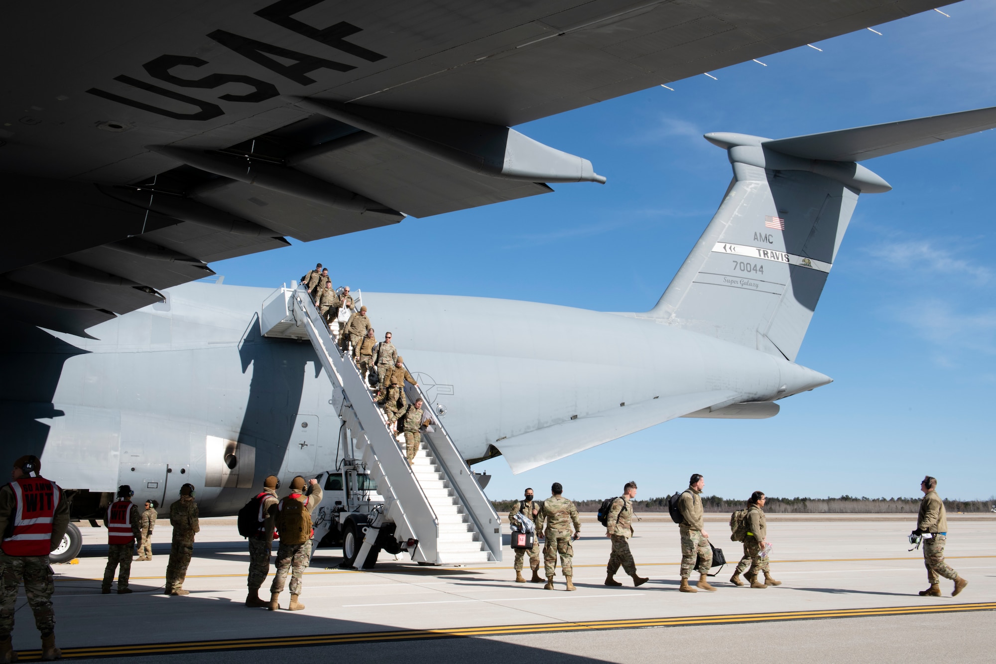 U.S. Airmen from the 60th Air Mobility Wing at Travis Air Force Base, California, arrive at the Alpena Combat Readiness Training Center, Alpena, Michigan, April 10, 2022, while exiting a C-5M Super Galaxy. There is a staircase at the tail end of the C-5 as the Airmen walk down it onto the flight line.
