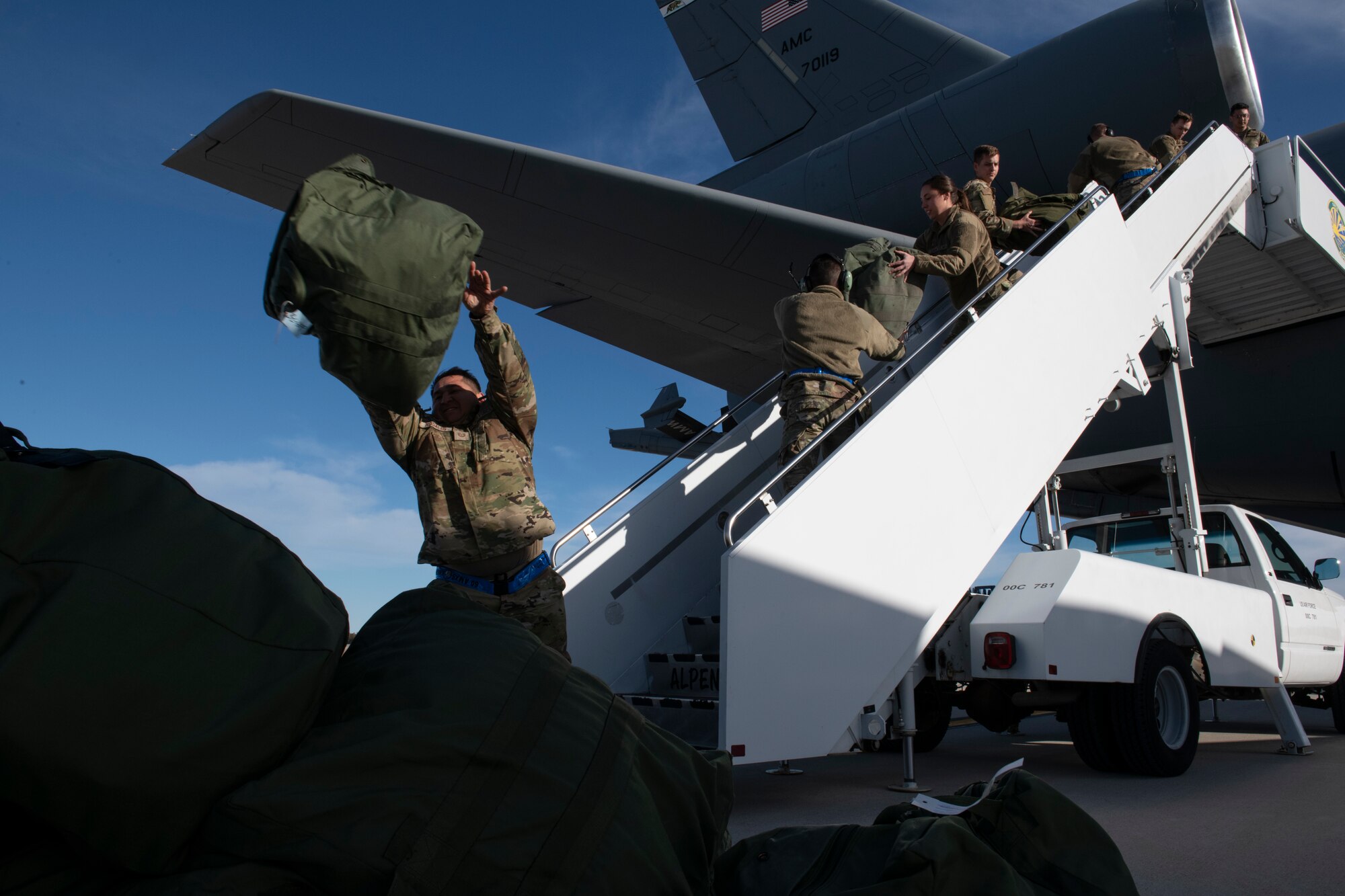 U.S. Airmen from the 60th Air Mobility Wing at Travis Air Force Base, California, off-load mission-oriented protective postures (MOPP) gear bags and luggage out of a KC-10 Extender from a staircase at the Alpena Combat Readiness Training Center, Alpena, Michigan, April 10, 2022.