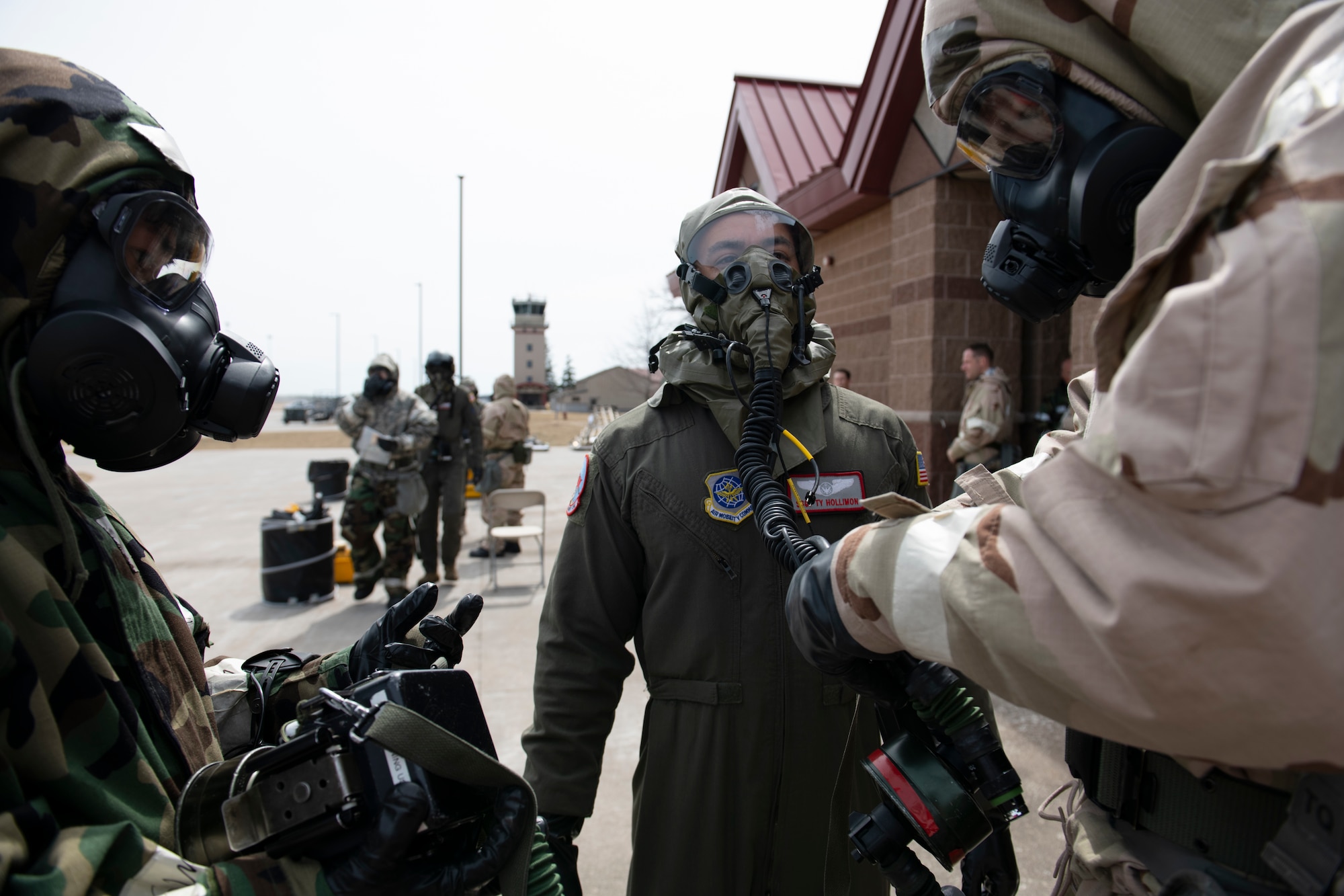 U.S. Airmen assigned to the 60th Air Mobility Wing, Travis Air Force Base, California, simulate the decontamination process through an aircrew contamination control area through after their arrival at the Alpena Combat Readiness Training Center, Alpena, Michigan, April 12, 2022. In the foreground, two Airmen are decontaminating an aircrew member. In the background, aircrew members are being processed.