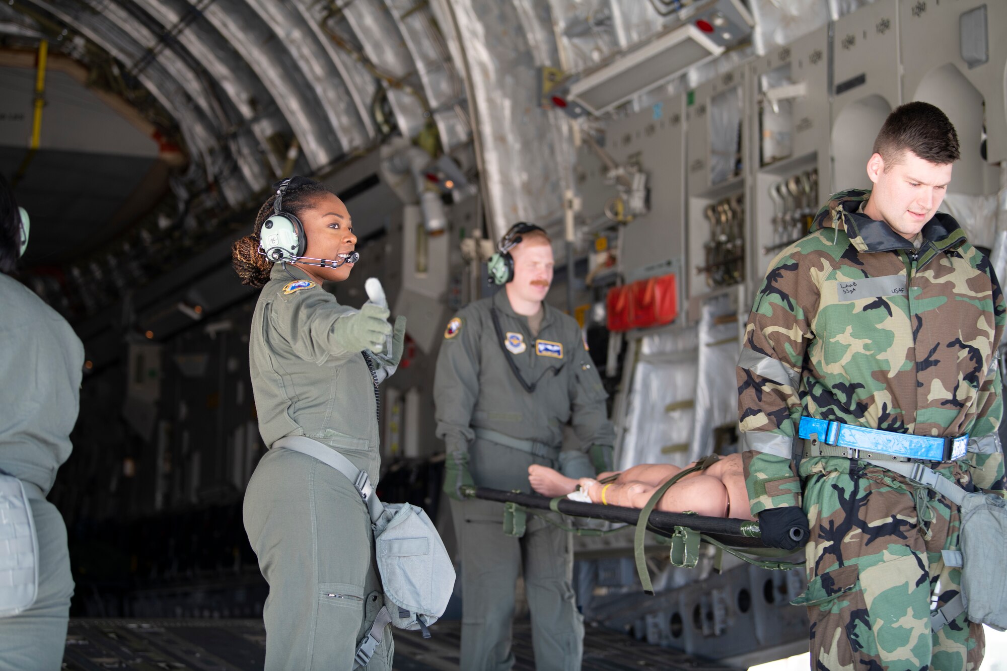 U.S. Air Force Major Angel Nwankwo, left, 60th Aeromedical Evacuation Squadron flight nurse, signals the off-load movement of a simulated patient from a C-17 Globemaster III at the Alpena Combat Readiness Training Center, Alpena, Michigan, April 12, 2022. The nurse is on the ramp of the C-17 as the simulated patient passes her.