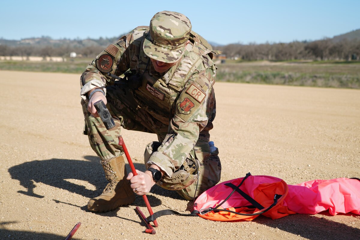 U.S. Air Force Tech. Sgt. Jeffrey Allen, assigned to the 146th Contingency Response Flight, hammers a stake into the ground to hold an improvised Rigging Alternate Method Zodiac for drop zone aircraft to use as a visual point of reference at Fort Hunter Liggett, California, Feb. 8, 2022. The 146 CRF and the 621st Contingency Response Wing partnered to accomplish skill-enhancing training for Allen's team while providing airlift support to the 621 CRW's evaluated exercise.