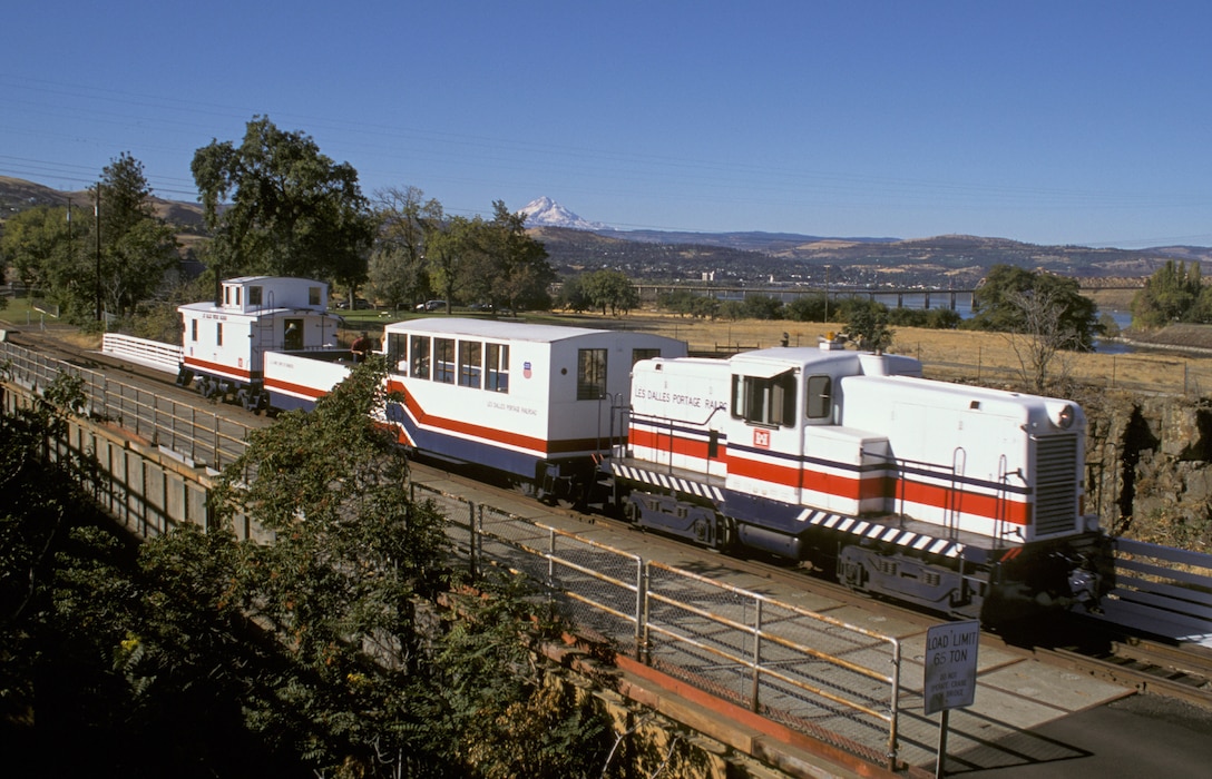 The fourth and final version of the Dalles Dam Tour Train consisted of a 44-ton General Electric locomotive, partially enclosed passenger car and a caboose, all painted in matching red, white and blue. Photo courtesy of L.A. Scrafford