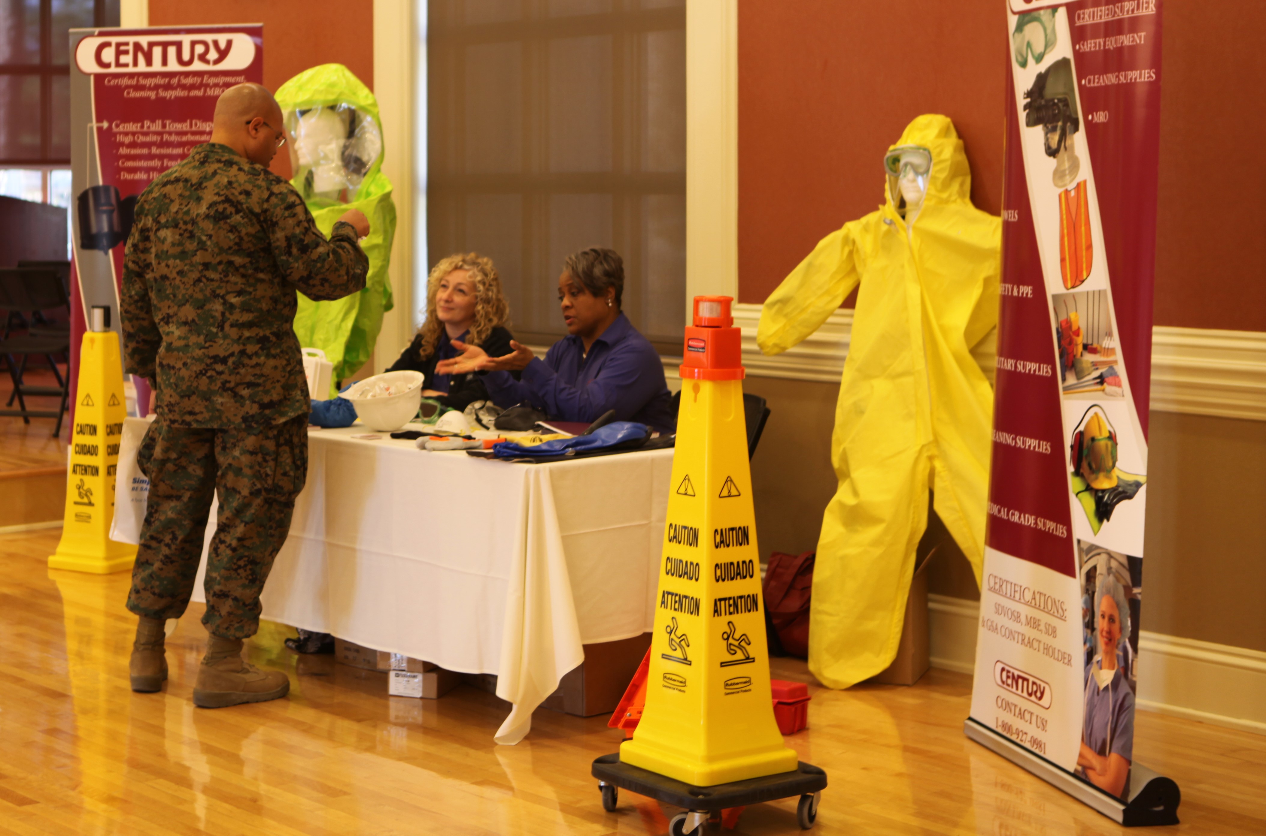 A Marine looking at a table with information about risk management. Two people sitting behind the table.