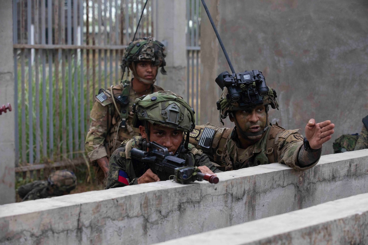 A soldier directs another soldier holding a gun.