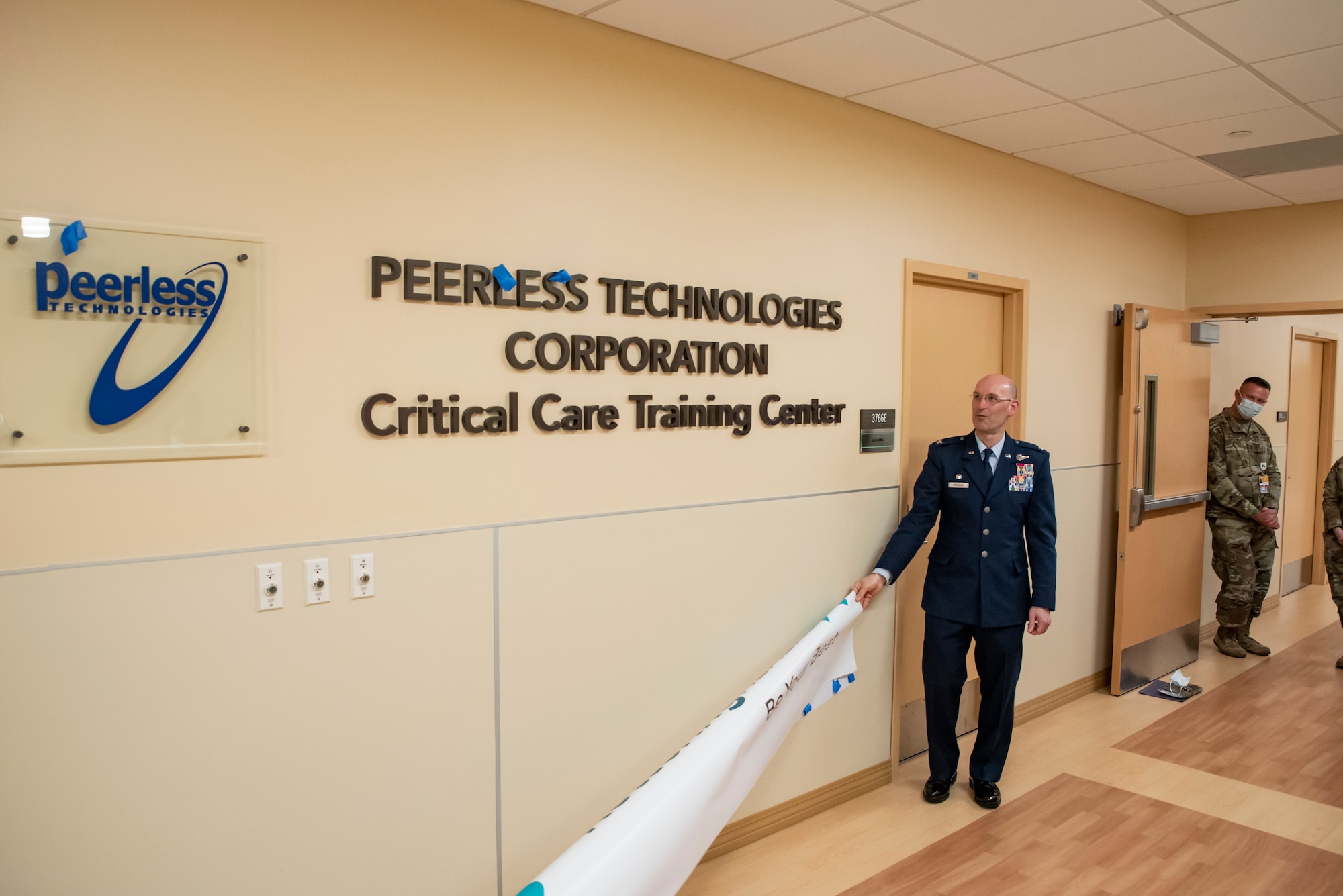 Col. Tory Woodard, center, commander, U.S. Air Force School of Aerospace Medicine, helps to reveal the new sign distinguishing the official opening of the Enlisted Critical Care Course (EECC) at the Soin Medical Center April 13, 2022, in Beavercreek, Ohio. USAFSAM is one of two mission units in the 711th Human Performance Wing, part of the Air Force Research Laboratory (AFRL). AFRL and Kettering Health Network partnered to create a training wing at Soin Medical Center, which allows the Air Force to received training as critical care technicians and also give back to the community. There are 10 courses in a year with 10 technicians each, and the four-week course provides didactics, lectures, simulations and real-patient care. (U.S. Air Force photo / Richard Eldridge)