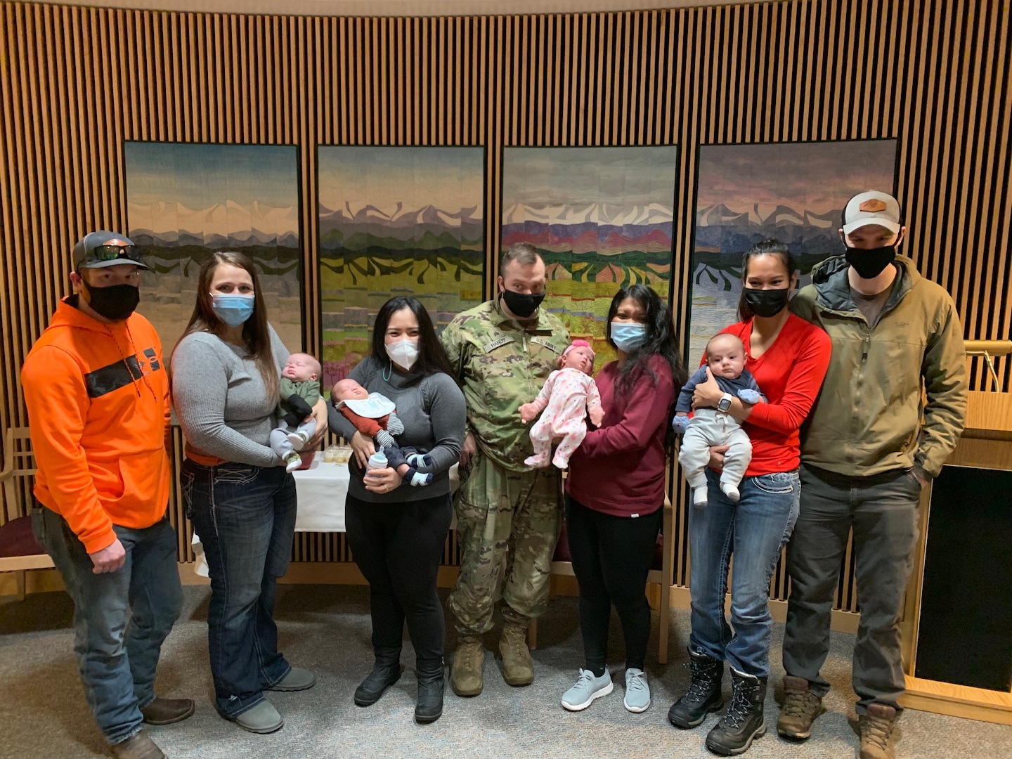 Seven adults and four infants standing in front of mountain scene quilts.