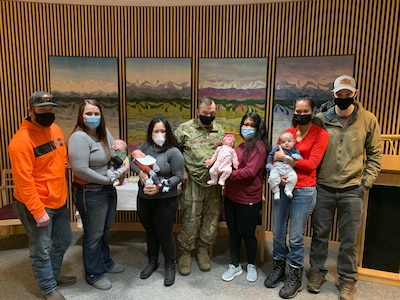 Women in gray sweaters holding infants with a woman in the background