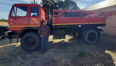 Fire Chief Ernie Glenn of the Minerva Volunteer Fire Department in Texas stands next to a former military truck. The truck has been converted into a fire truck and painted red.
