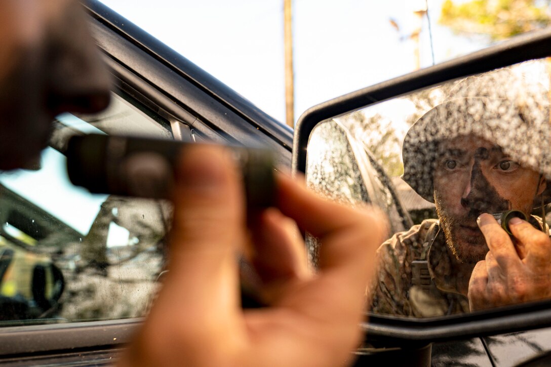 An airman puts on face paint on while looking at himself in the mirror.