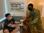 Man in shorts and tshirt sitting down receiving a meal tray from a soldier.