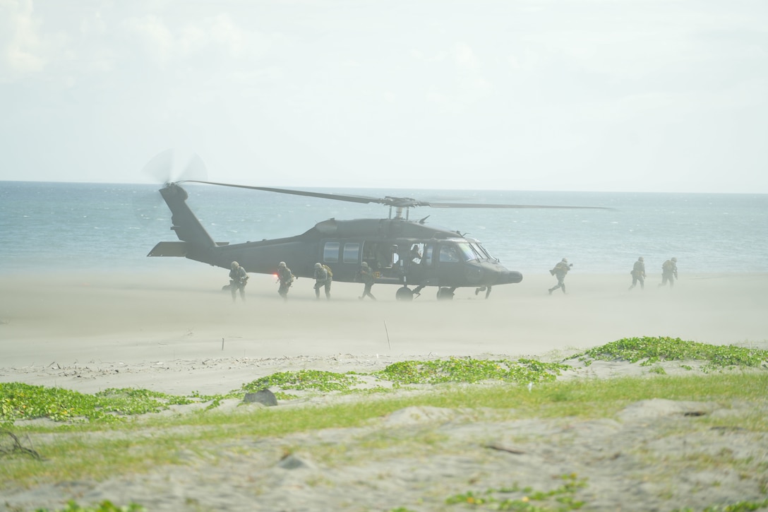 Marines jump from a helicopter onto a beach.