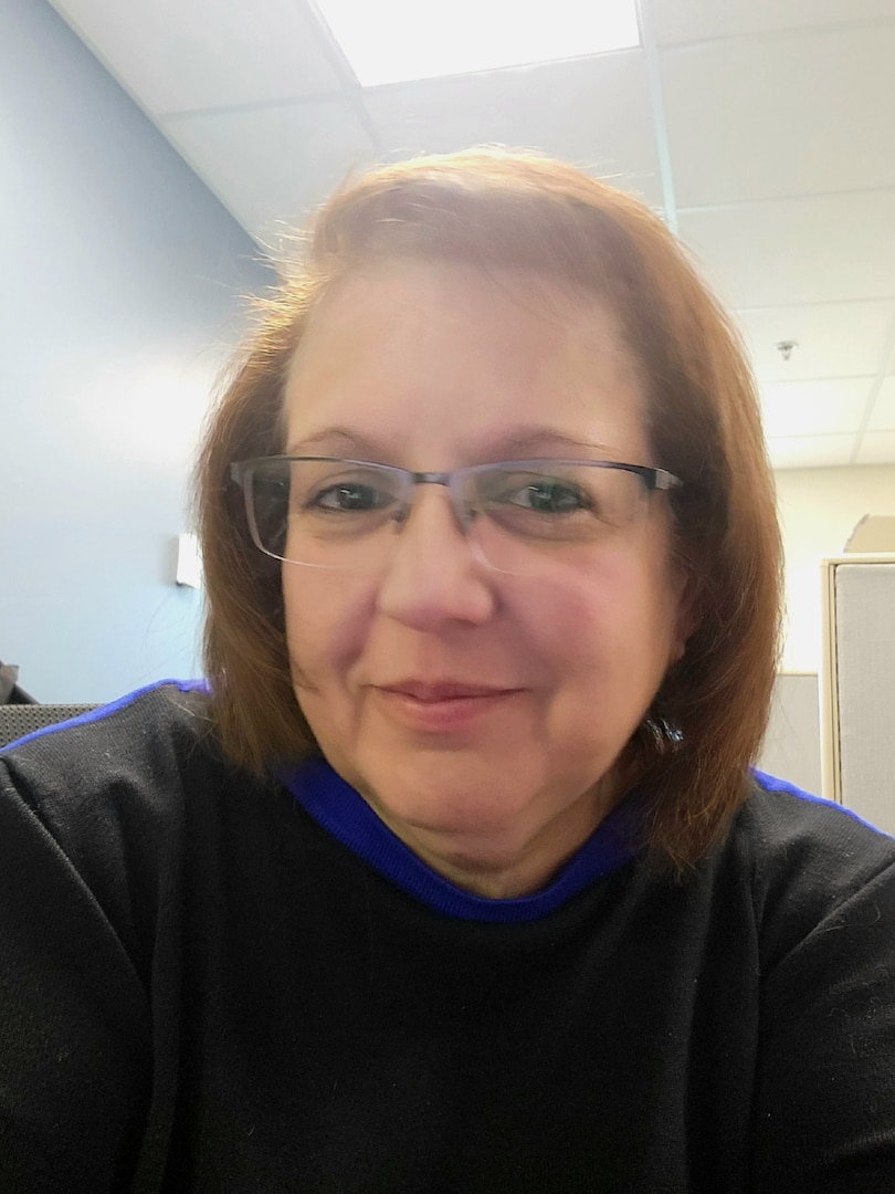 A woman, Ramona Ross, looks into the camera while sitting at her workstation.