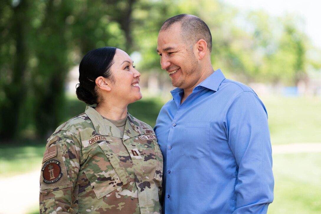 An airman and her spouse smile and look at each other while standing outside for a photo.