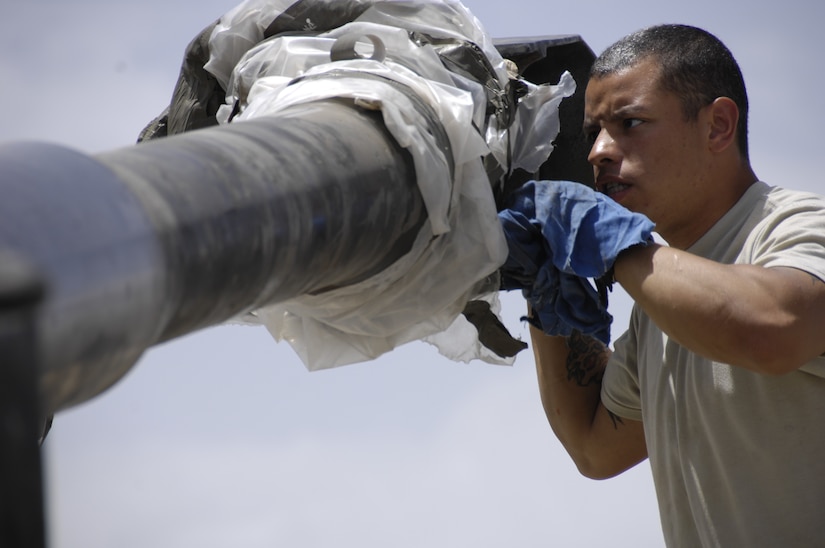 A soldier interacts with the barrel of a large gun.