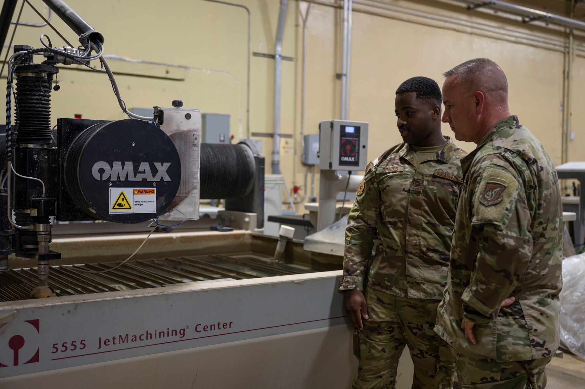 U.S. Air Force Chief Master Sgt. David R. Wolfe, Pacific Air Forces command chief, is briefed by an Airman with the 36th Maintenance Group on a water jet cutter at Andersen Air Force Base, Guam, April 14, 2022.