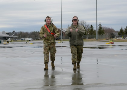 U.S. Air Force Senior Airman Kyle Pamperin and Staff Sgt. Marcel Emond, both crew chiefs assigned to the Wisconsin Air National Guard's 115th Fighter Wing, Madison, Wisconsin, give a thumbs up while walking on the flight line of the Vermont Air National Guard's 158th Fighter Wing, Burlington, Vermont April 13, 2022. Pamperin and Emond have been training on the F-35 Lightning II as a crew chief at the 158th Fighter Wing in Burlington for just over a year as part of the 115th Fighter Wing's transition from the F-16 Fighting Falcon to the F-35. (U.S. Air National Guard photo by Staff Sgt. Cameron Lewis)