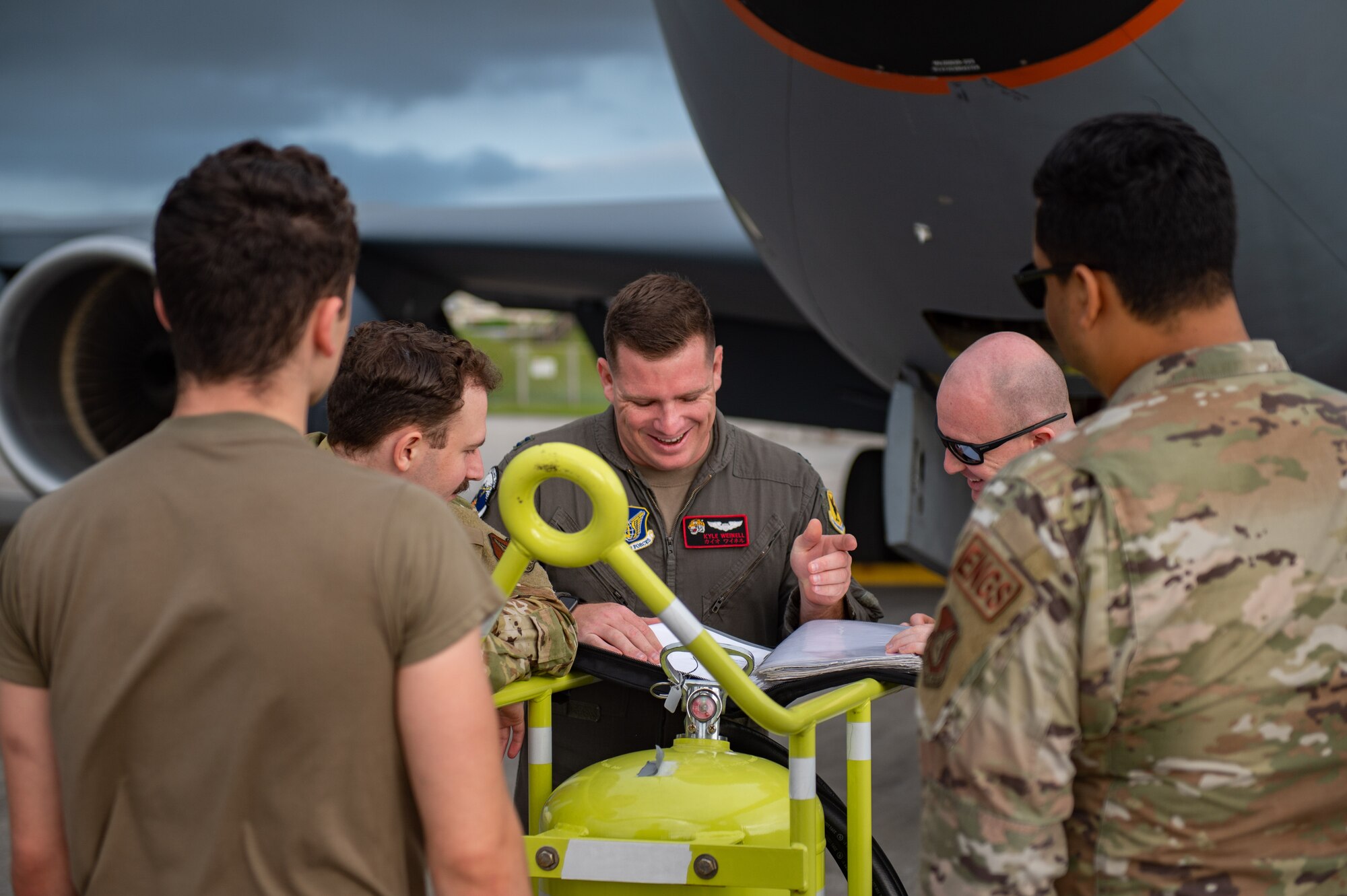 A group of airmen gather for a preflight brief in front of a plane.