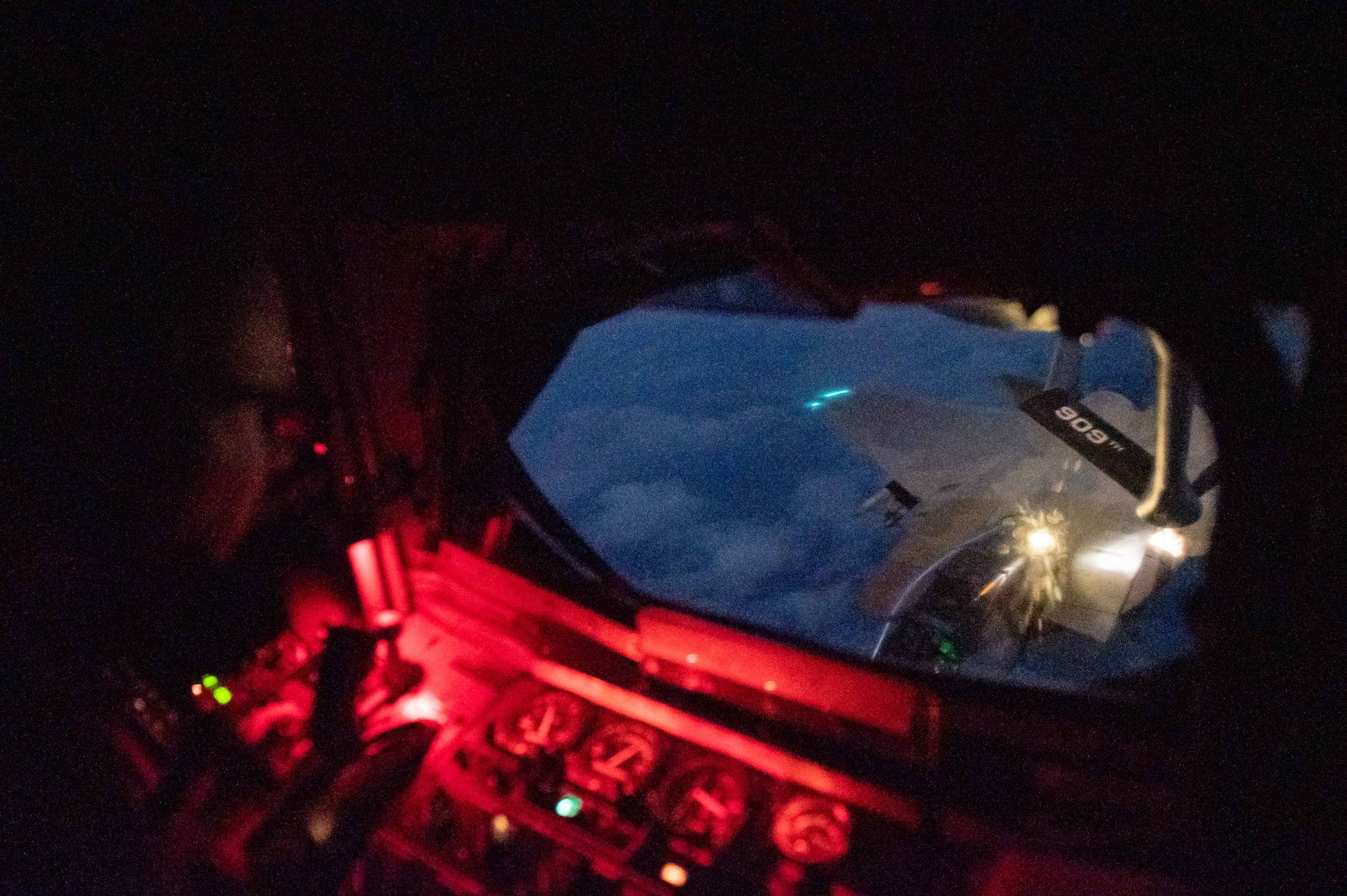 A boom operator refuels a fighter jet at night