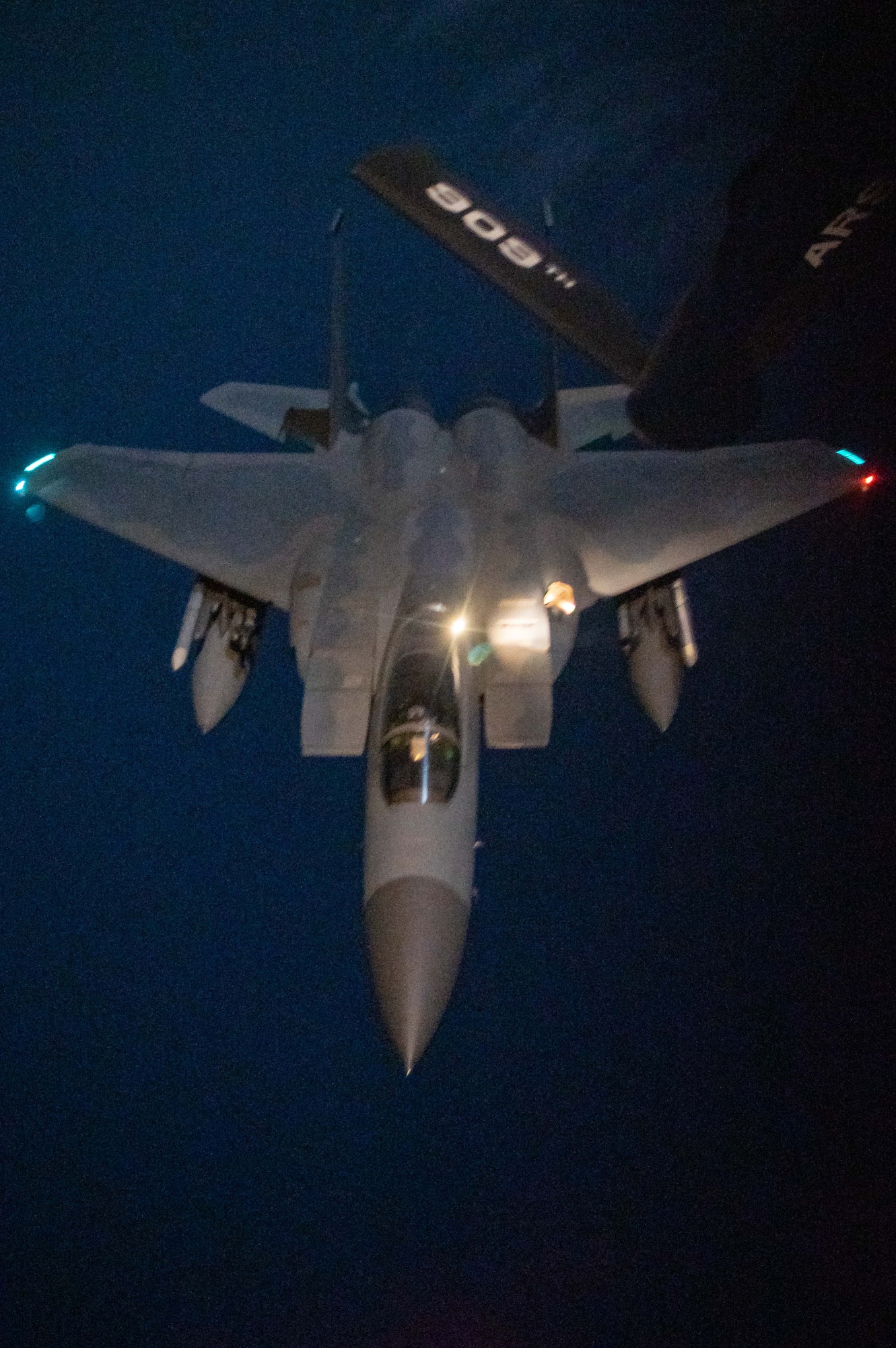 A fighter jet flies underneath a refueling plane at night