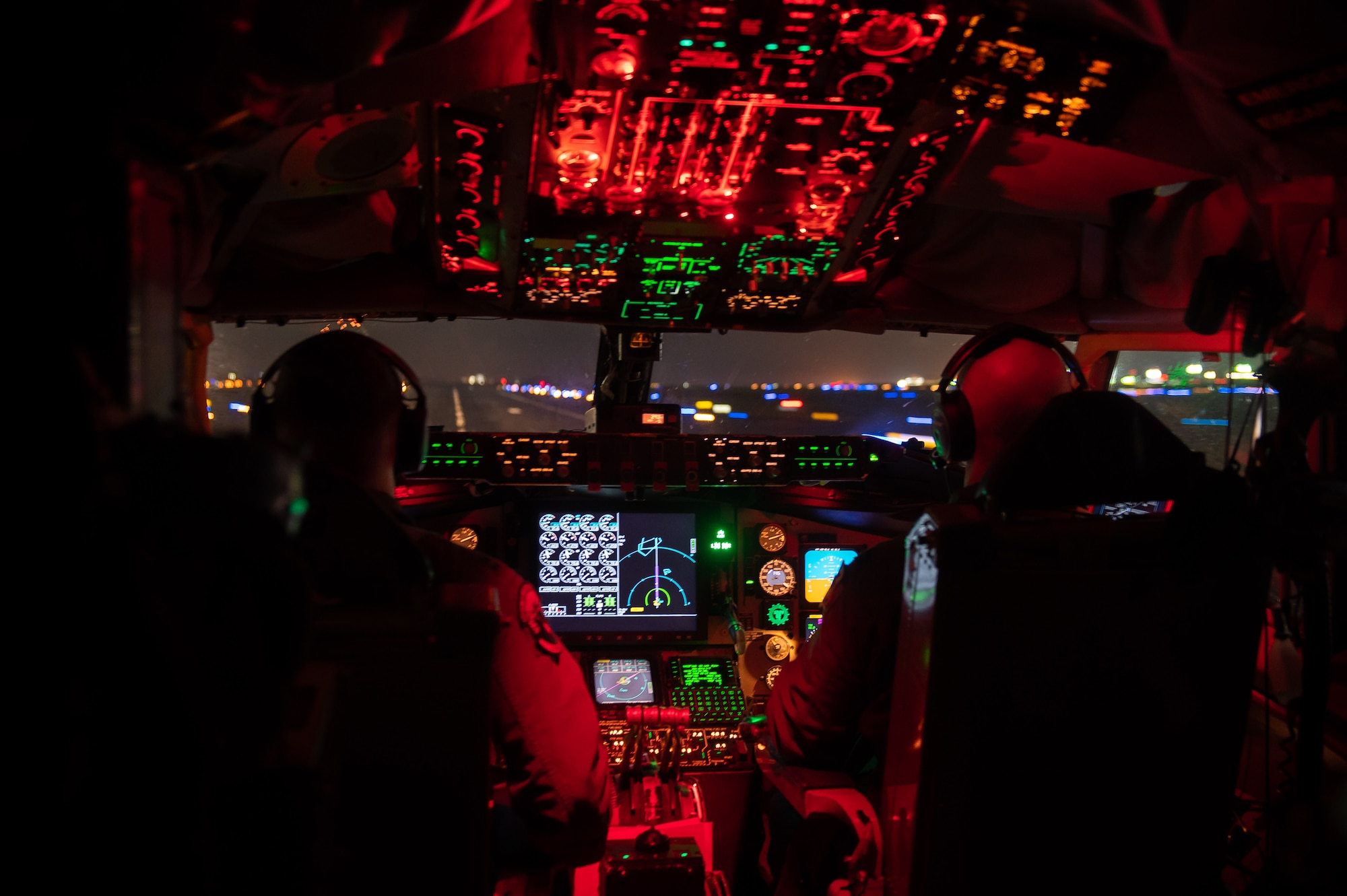 A cockpit is lit up red as two pilots land a plane