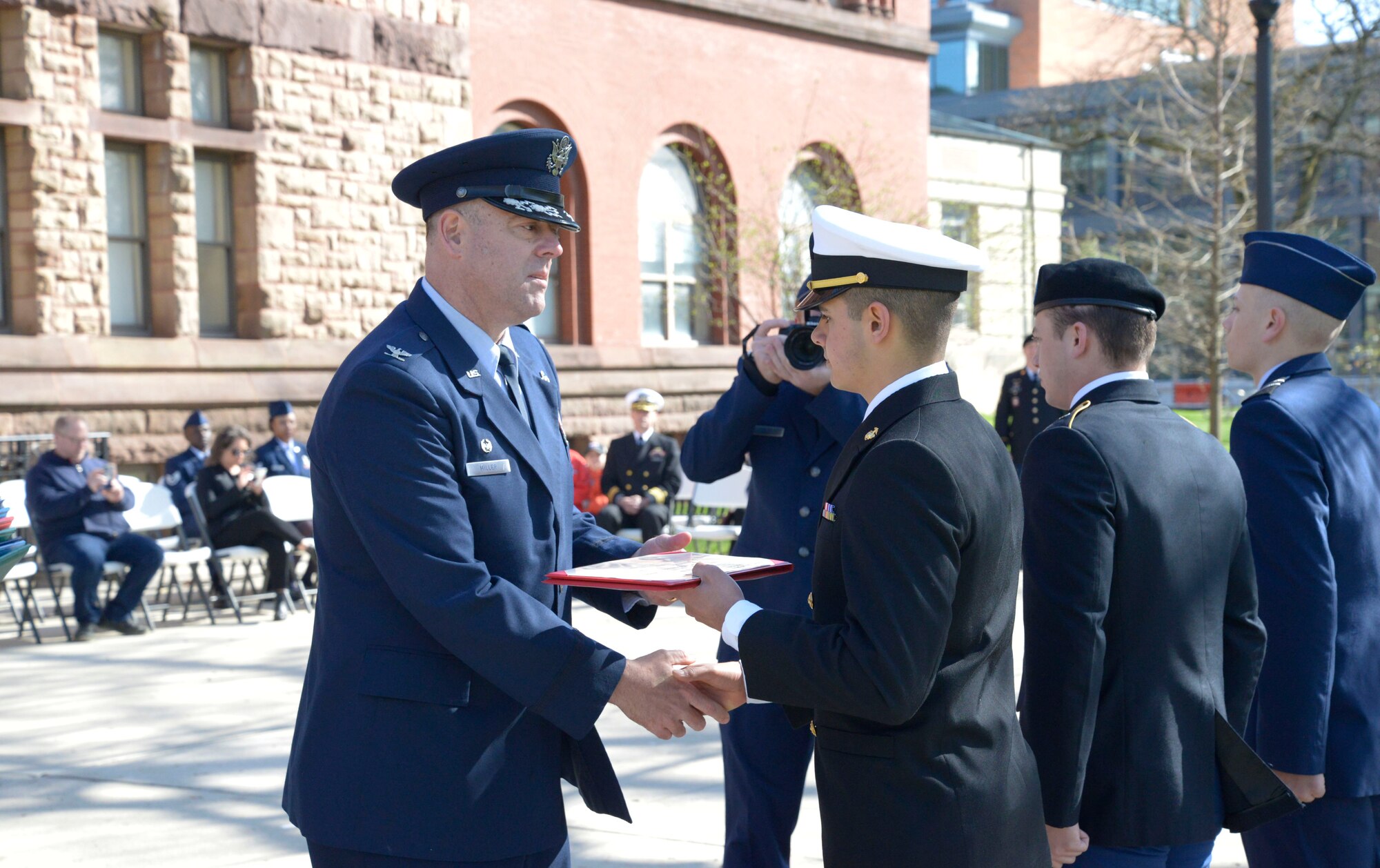 Col. Patrick Miller, 88th Air Base Wing and Wright-Patterson Air Force Base commander, awards Navy ROTC midshipman Colin Patil the Major Lawrence scholarship April 14, 2022 at Ohio State University. The Tri-Service Parade has been a tradition at Ohio State University since 1916, and allows several cadets and midshipmen to receive scholarship awards from generous donors. (U.S. Air Force photo by Darrius Parker)