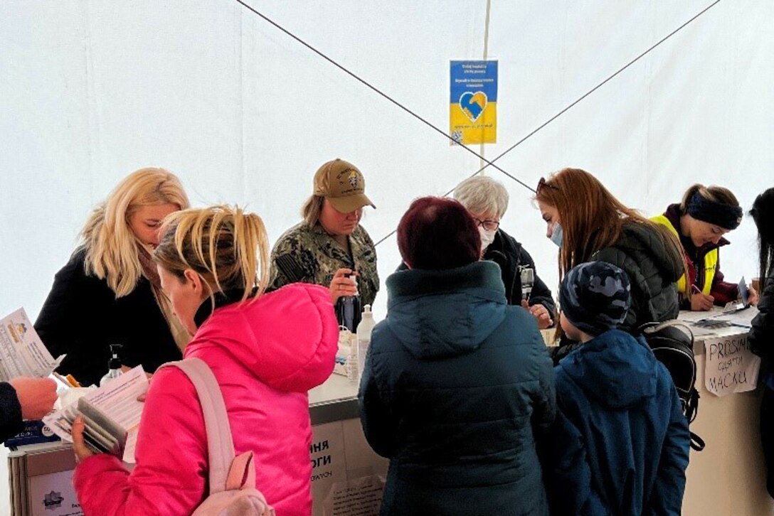 Families are lined in front of a table filling out paperwork across from personnel.