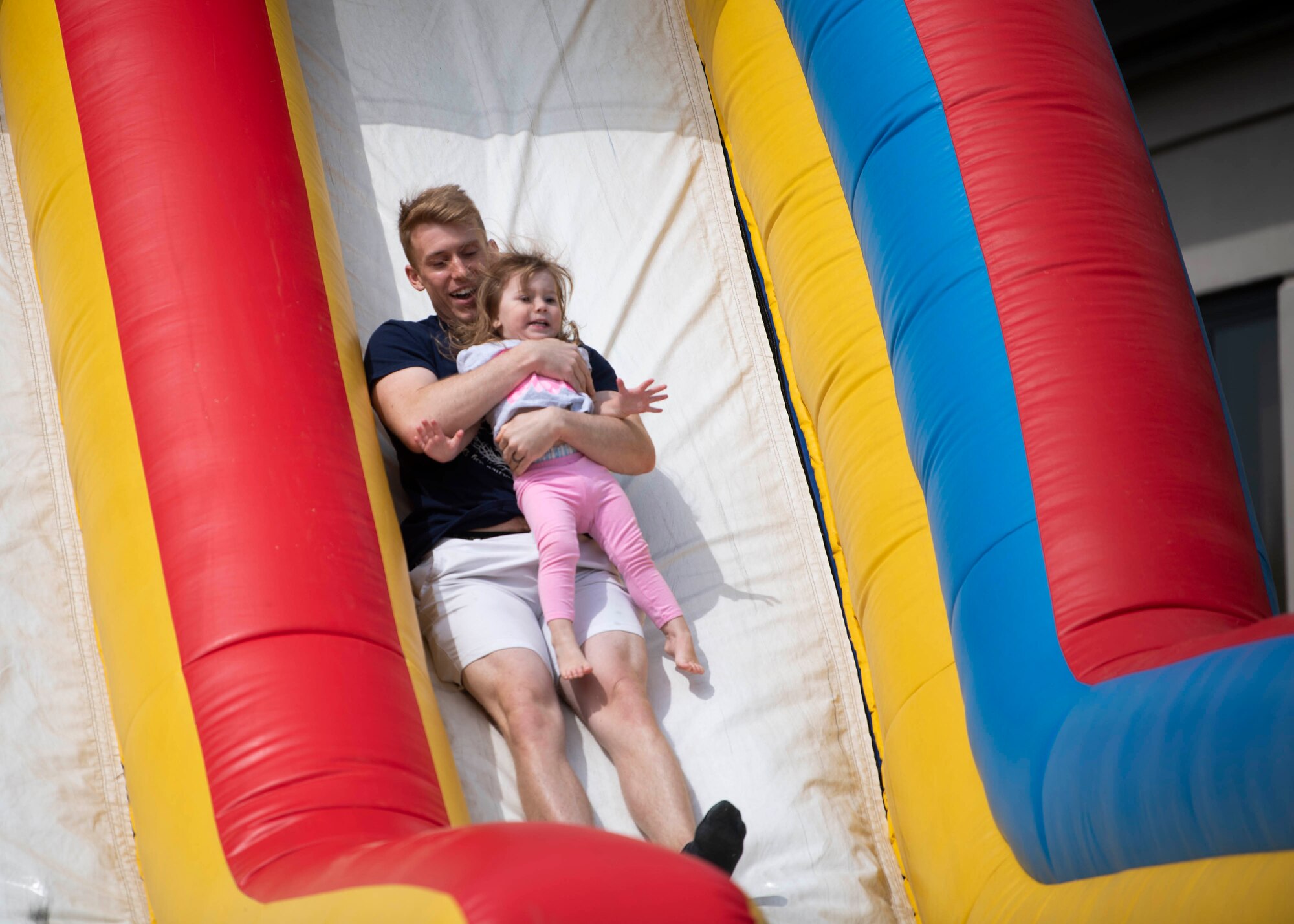 Senior Airman Michael Satterfield, 436th Aircraft Maintenance Squadron crew chief, slides down an inflatable slide with his daughter, Cora, 2, during the Easter Egg-stravaganza at Dover Air Force Base, Delaware, April 16, 2022. Hosted by the Dover AFB Chaplain Corps and the USO, the event featured a bounce house and slide, Easter egg hunt, free food and raffle. (U.S. Air Force photo by Tech. Sgt. J.D. Strong II)