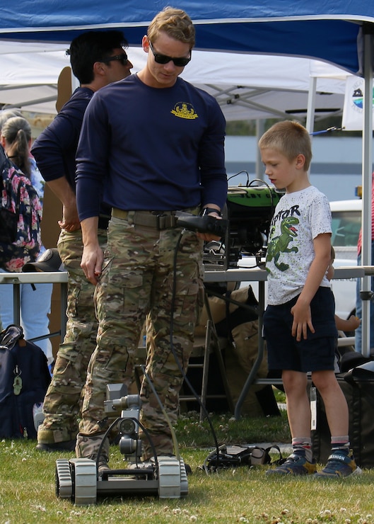 A service member, assigned to Detachment Northwest, Explosive Ordnance Disposal Mobile Unit 11, teaches a child how to navigate an unmanned ground vehicle during a National Night Out at Windjammer Park in Oak Harbor, Washington Aug. 3, 2021. National Night Out is an annual community-building campaign designed to enhance the relationship between neighbors and law enforcement. National Night Out was introduced in August of 1984 through an already established network of law enforcement agencies, neighborhood watch groups, civic groups, state and regional crime prevention associations, and volunteers across the nation.
