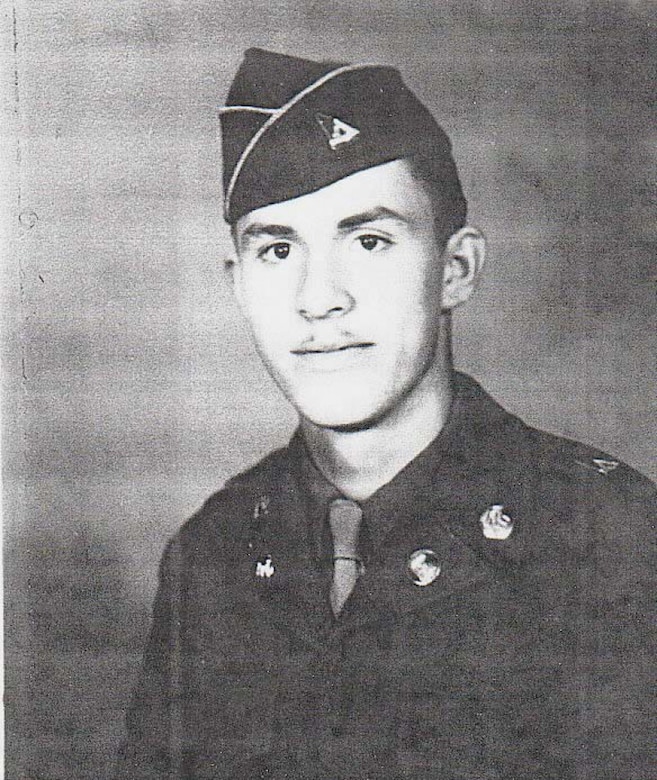 A young man in uniform and a cap poses for a photo.