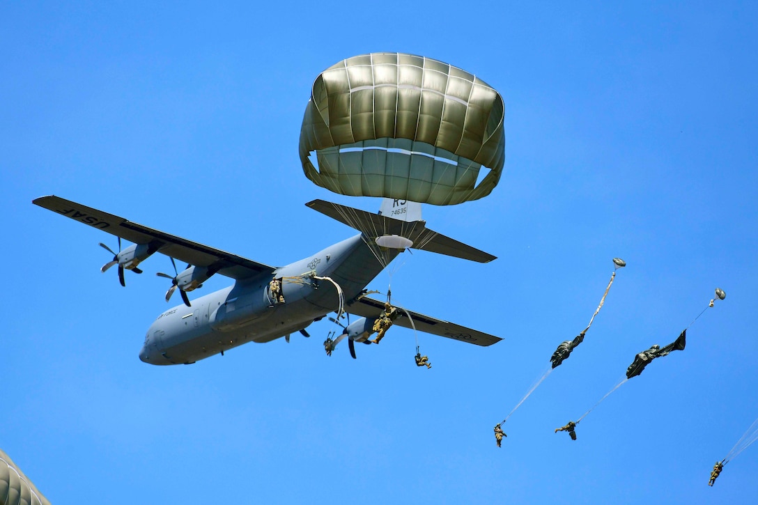 Soldiers jump from an airborne aircraft while wearing parachutes.