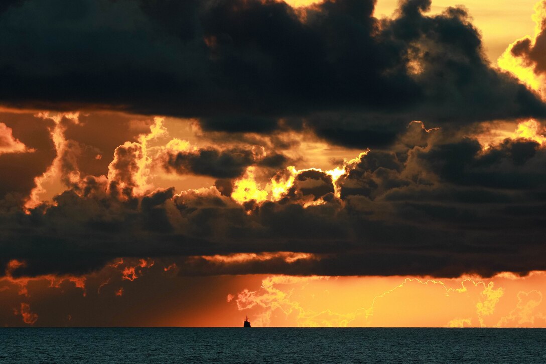 A ship sails under a dramatic orange sky streaked with dark clouds.