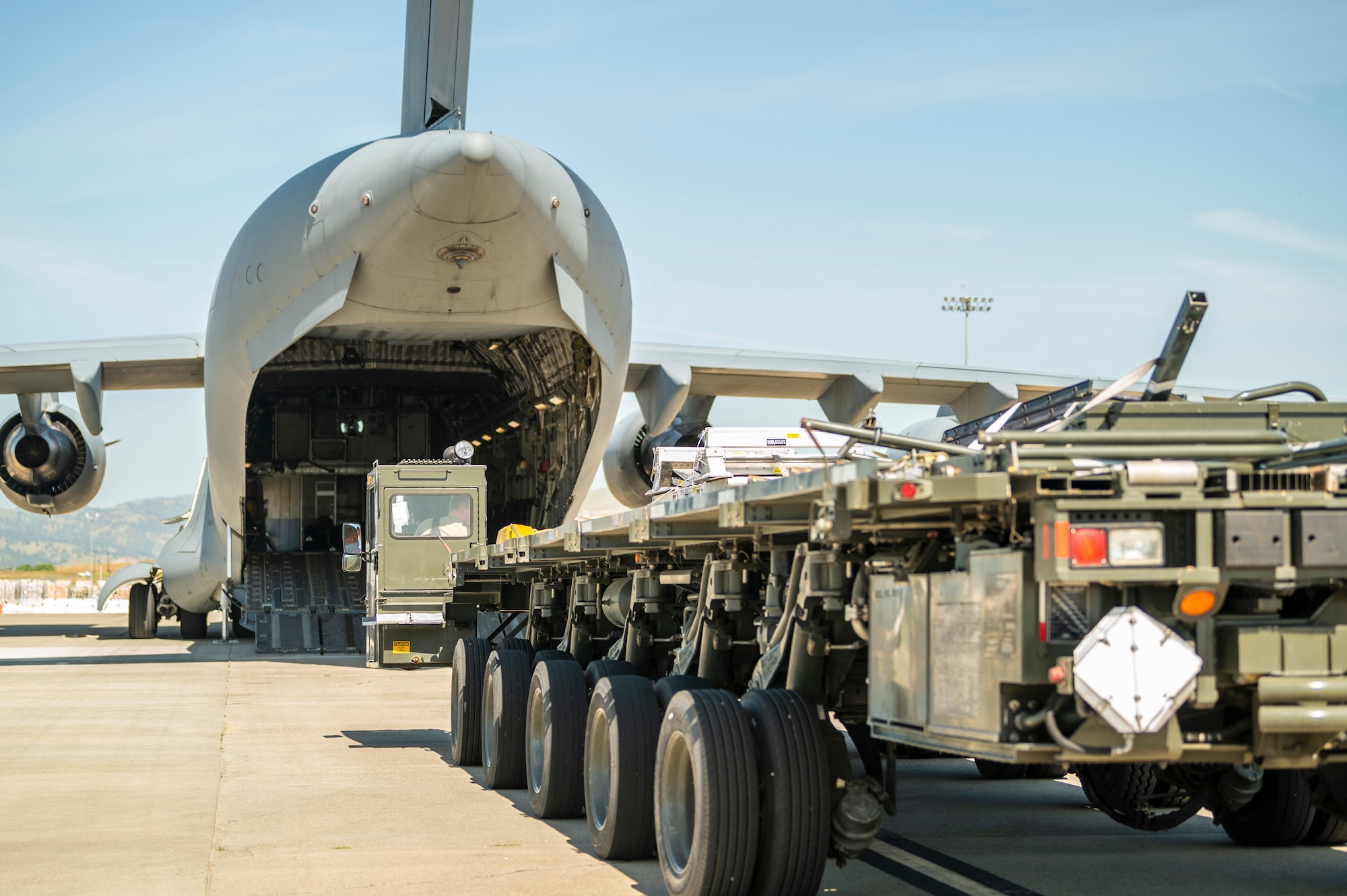 A large military vehicle that is used to load pallets on to large military aircraft, drives towards  a C-17 Globemaster III, a large Air Force aircraft.