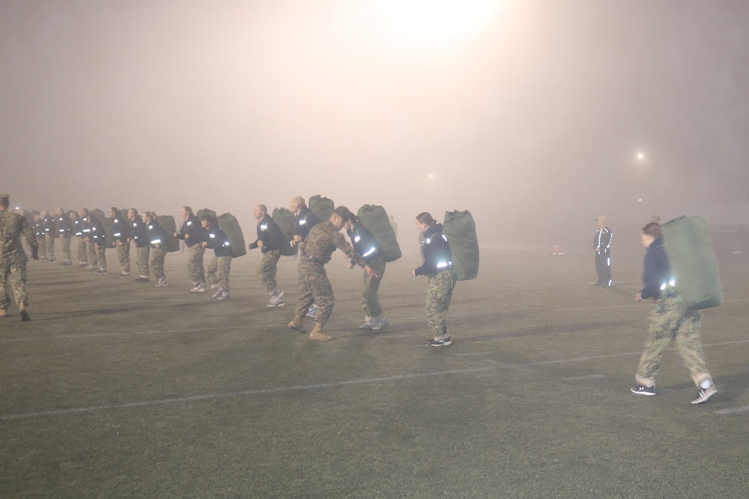Service members get in formation on a foggy sports field.