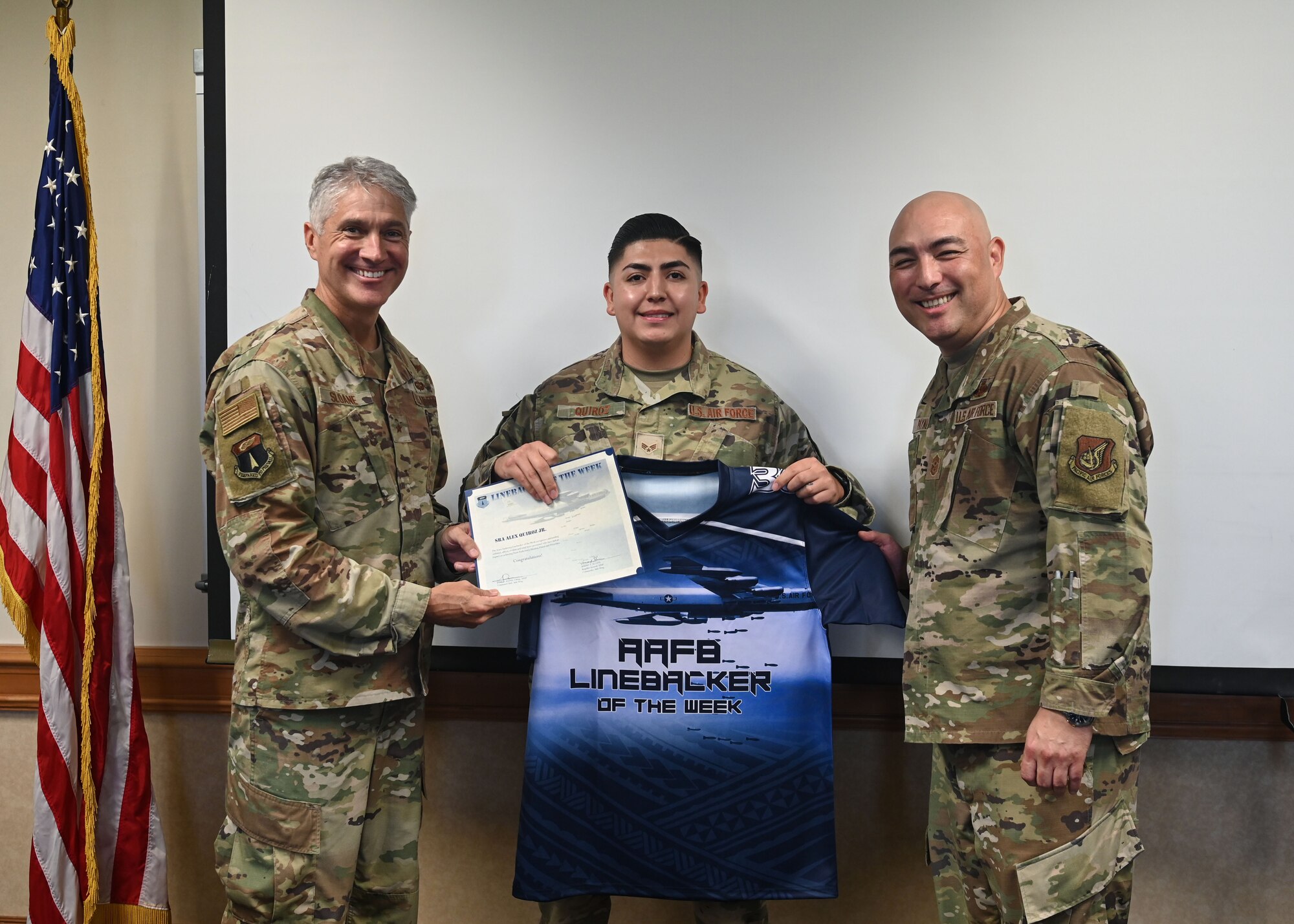 U.S. Air Force Senior Airman Alex Quiroz Jr., a Base Defense Operations Center Controller with the 36th Security Force Squadron, is presented a certificate and jersey from U.S. Air Force Brig. Gen. Jeremy Sloane, 36th Wing commander, and U.S. Air Force Chief Master Sgt. John Payne, 36th Wing command chief, for the Linebacker of the Week award at Andersen Air Force Base, Guam, April 13, 2022.