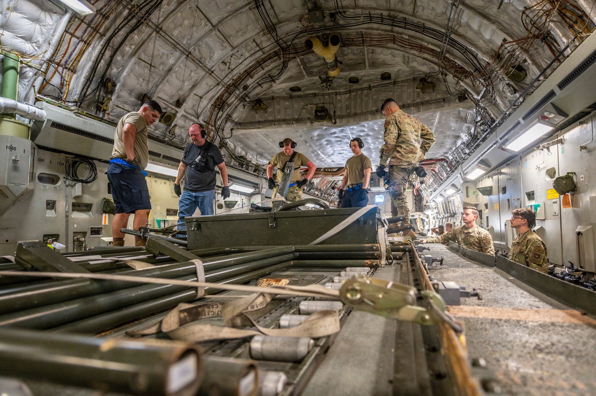 A group of men are around a large military vehicle that is used to load pallets on to large military aircraft, in side of a C-17 Globemaster III, a large Air Force aircraft.