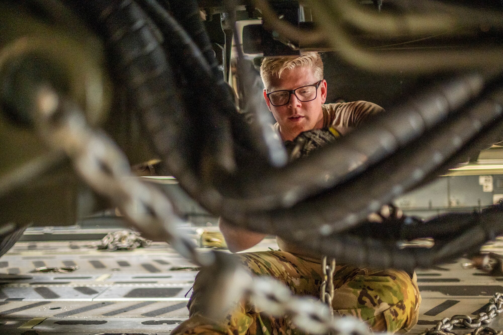 A man straps in a large military vehicle that is used to load pallets on to large military aircraft, in side of a C-17 Globemaster III, a large Air Force aircraft.