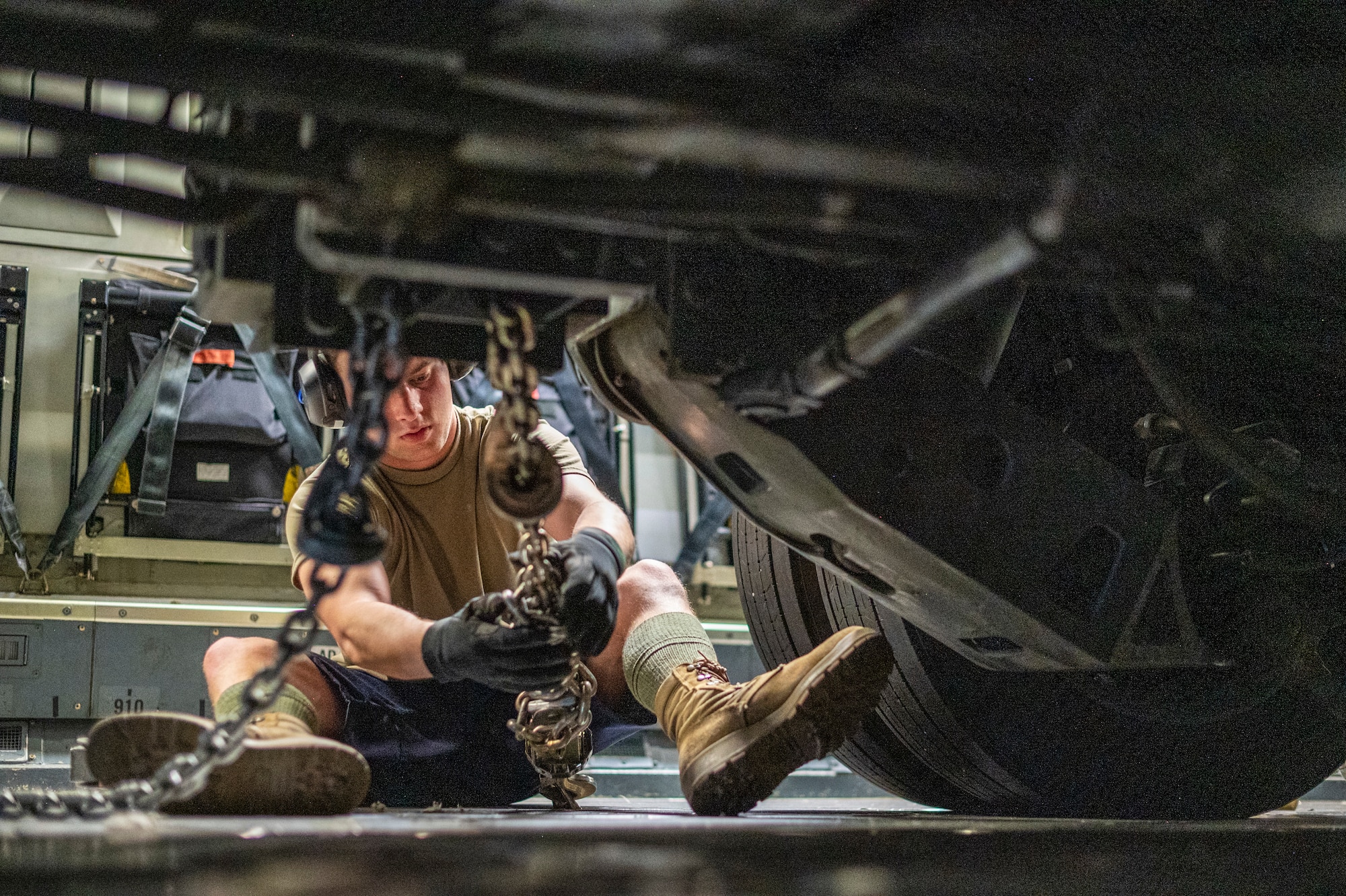 a man straps in a large military vehicle that is used to load pallets on to large military aircraft, in side of a C-17 Globemaster III, a large Air Force aircraft.