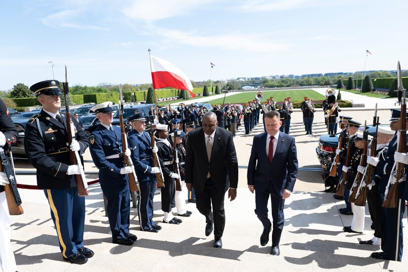 Two men walk up some steps with service members on each side.